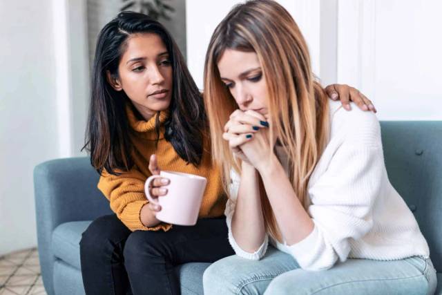 Femme soutenant une autre femme assise, une main sur son épaule.