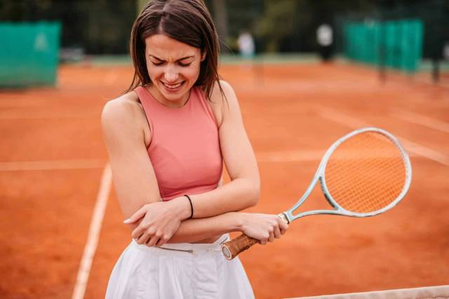 Femme en tenue de tennis tenant son coude.