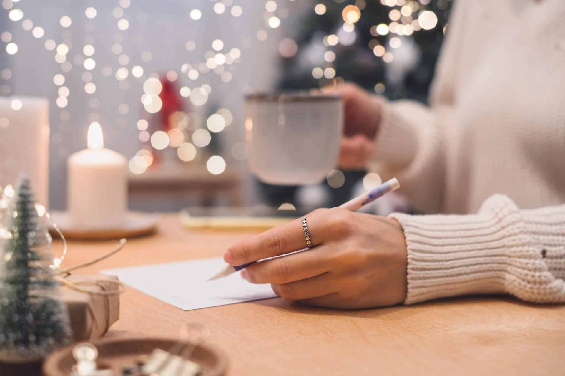 Personne écrivant sur une feuille près d’une tasse et de décorations de fêtes.