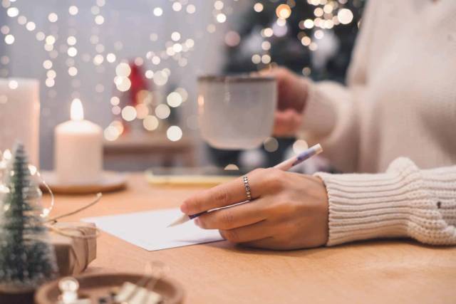 Personne écrivant sur une feuille près d’une tasse et de décorations de fêtes.