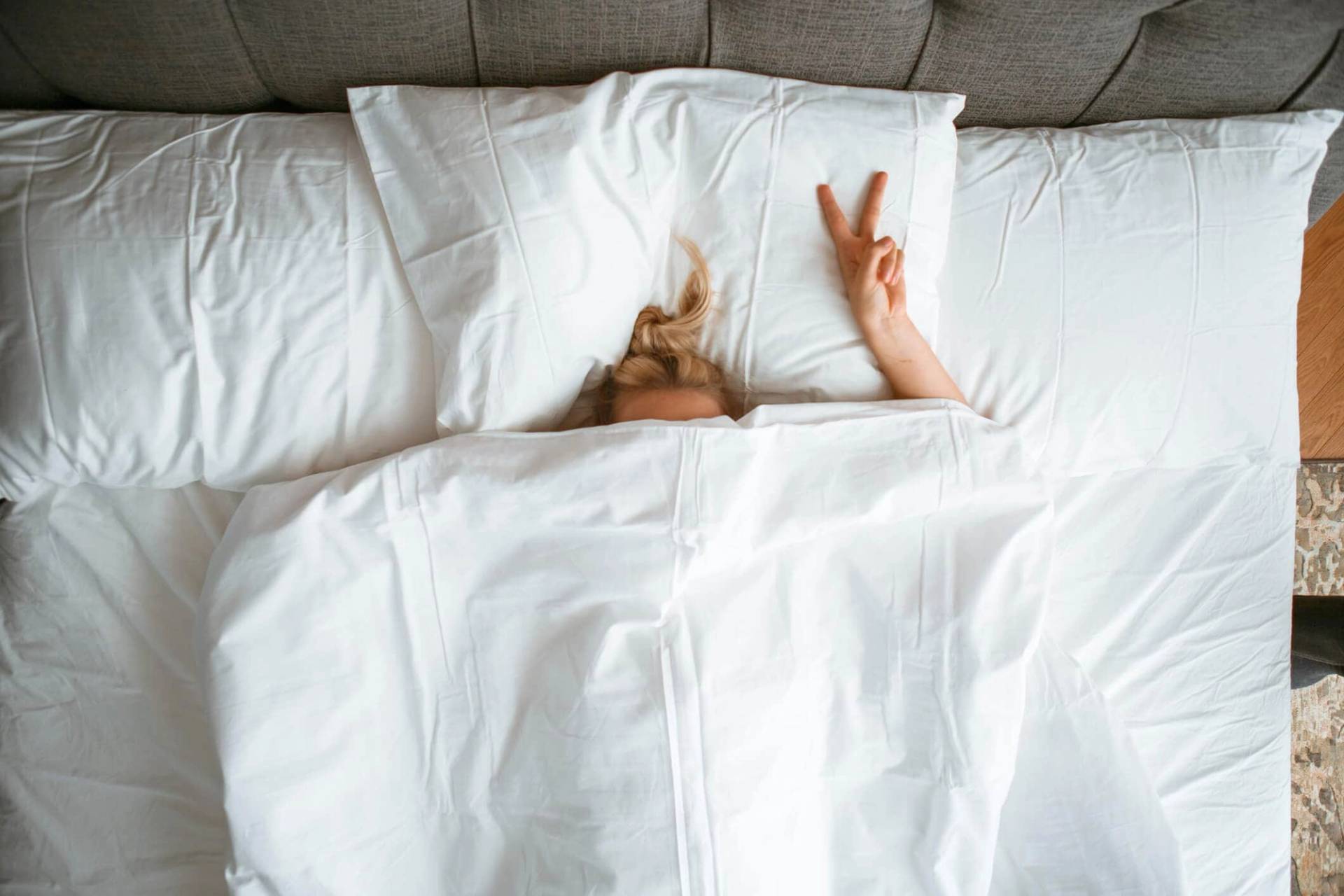 Personne cachée sous une couette, une main levée.