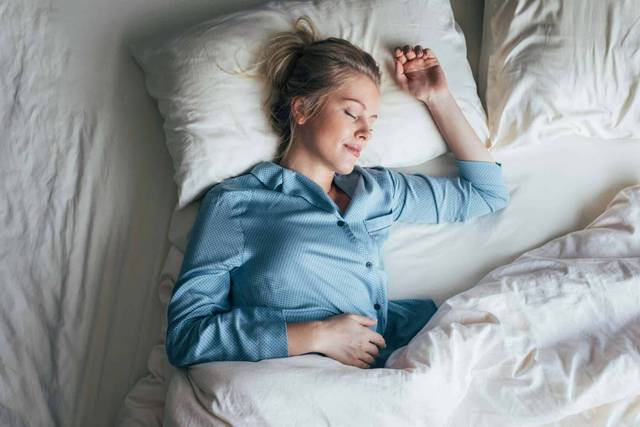 Femme dormant paisiblement dans son lit, illustration du sommeil réparateur et de la qualité du repos