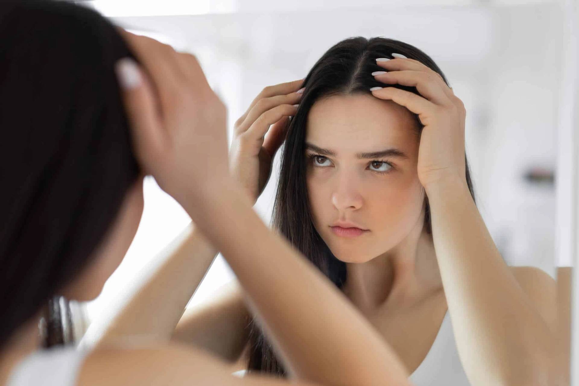 Femme examinant ses cheveux devant un miroir.