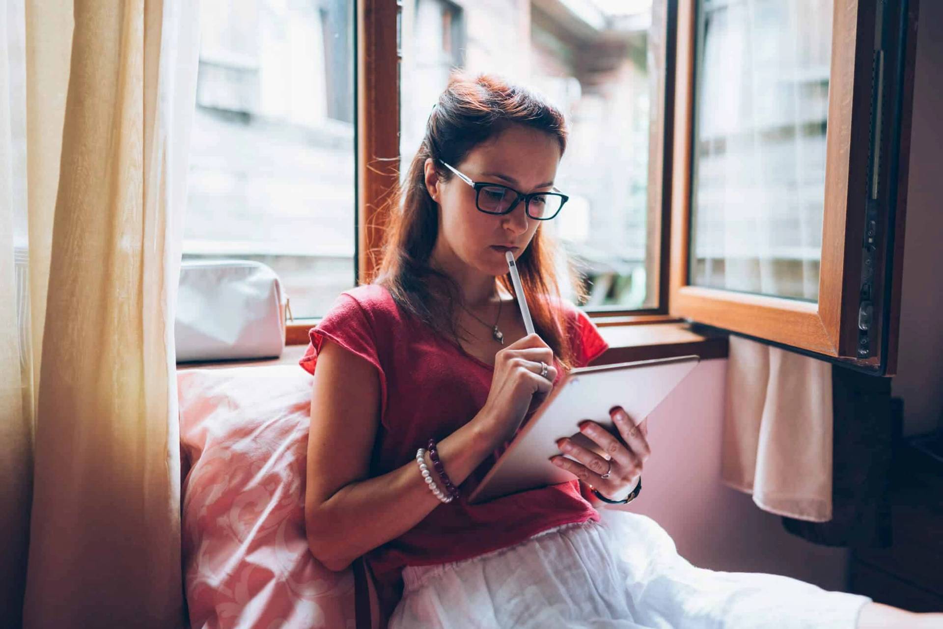 Femme assise sur un lit tenant une tablette.