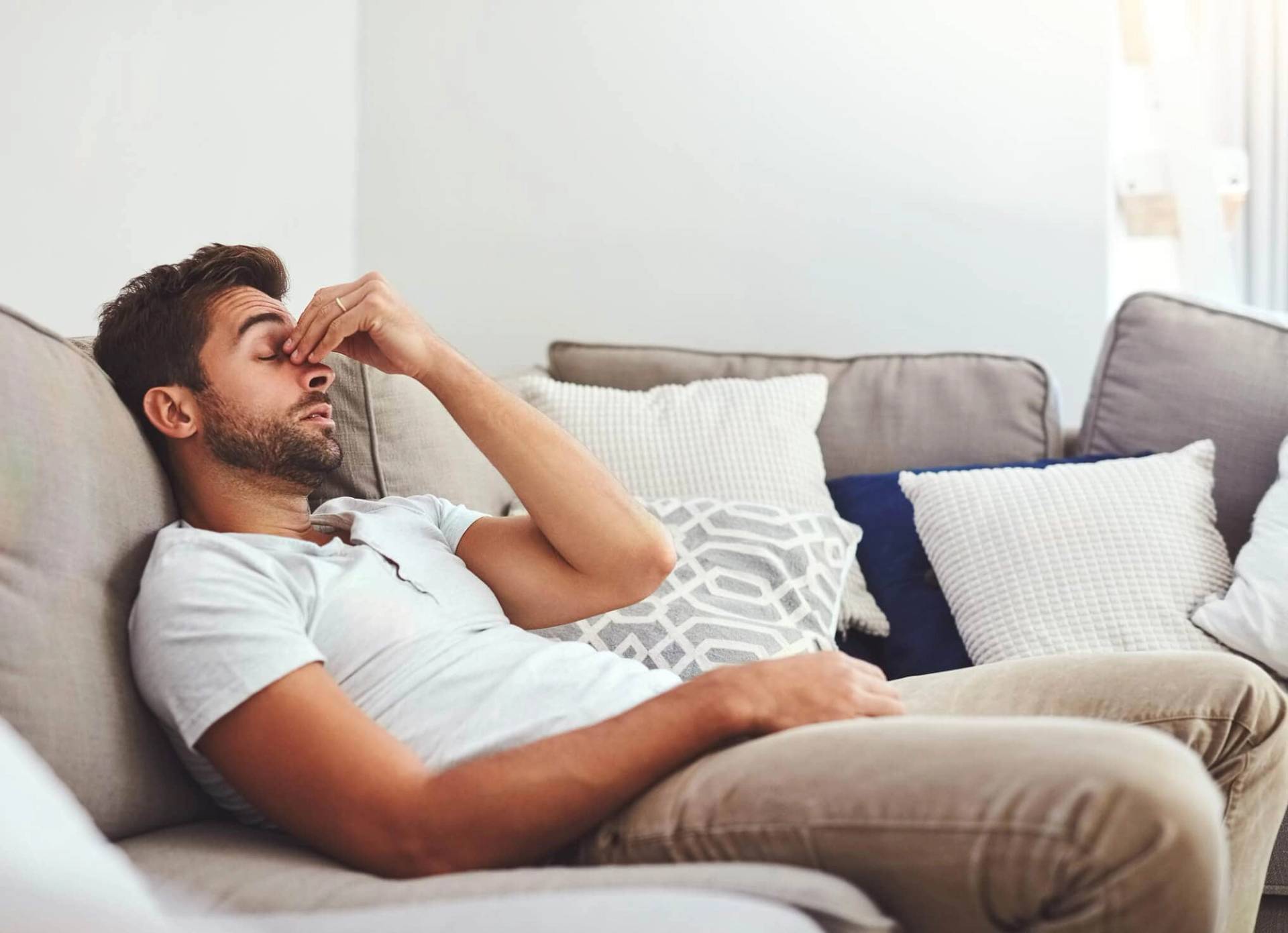 Homme allongé sur un canapé avec une main près du nez.
