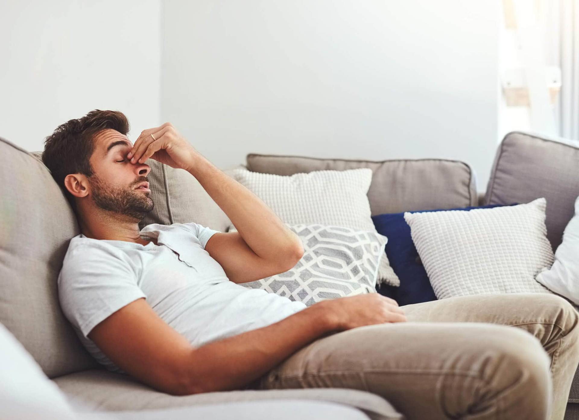 Homme allongé sur un canapé avec une main près du nez.