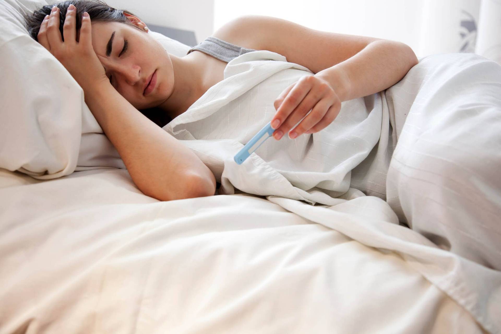 Femme allongée dans un lit regardant un thermomètre.