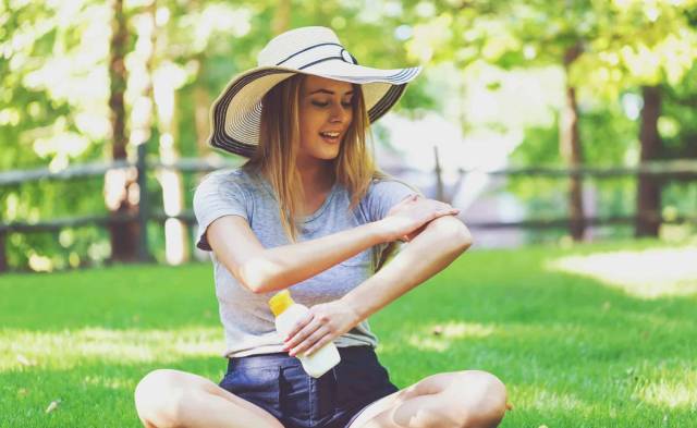 Femme portant un chapeau et appliquant de la crème sur son bras dans un jardin.