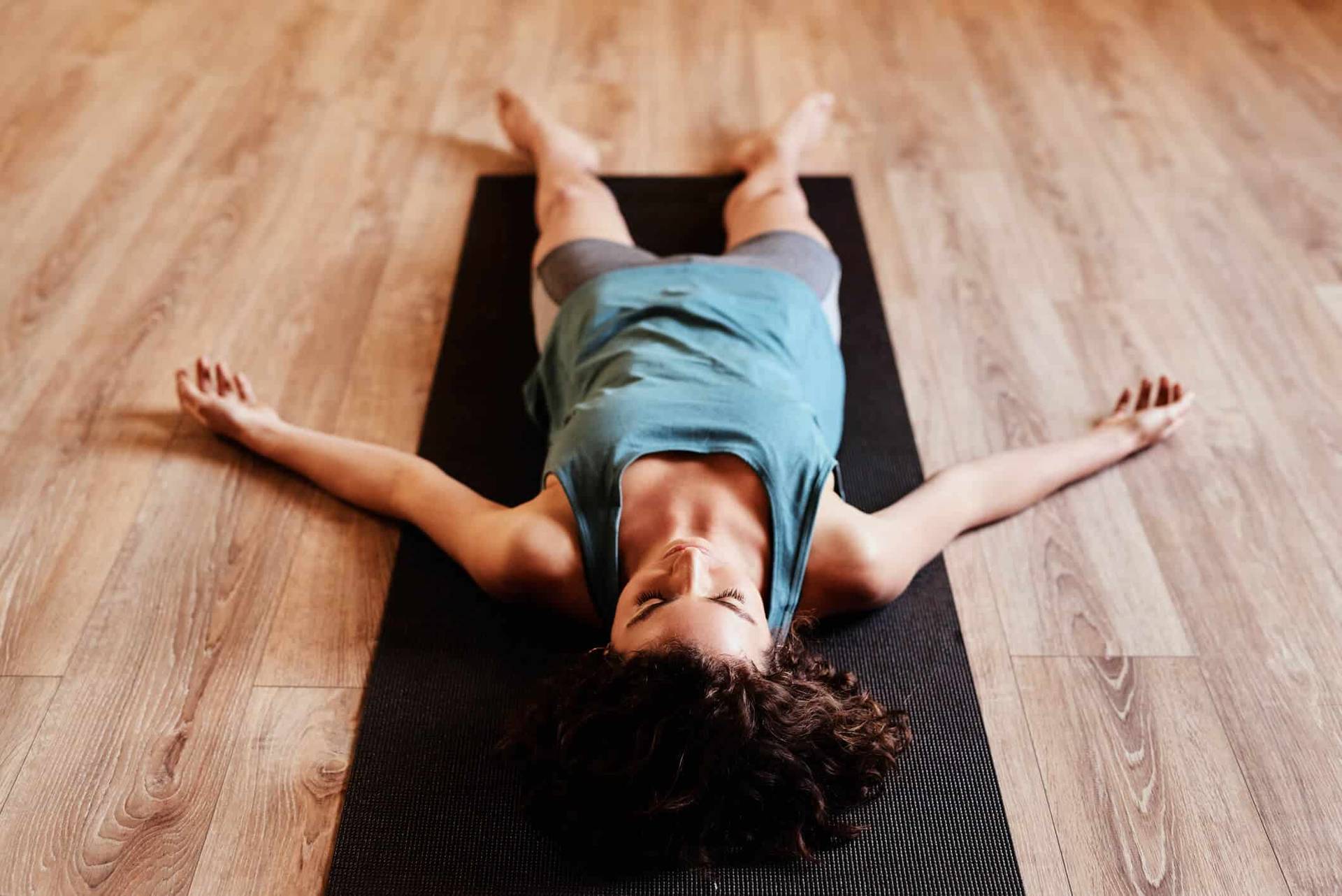Femme allongée sur un tapis de yoga, bras écartés.