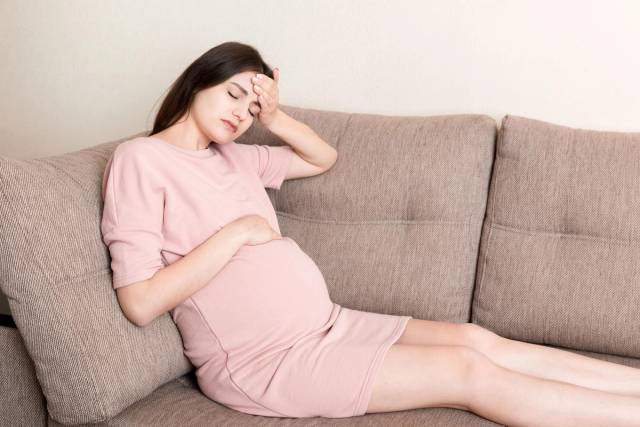 Personne enceinte allongée sur un canapé, une main sur la tempe.