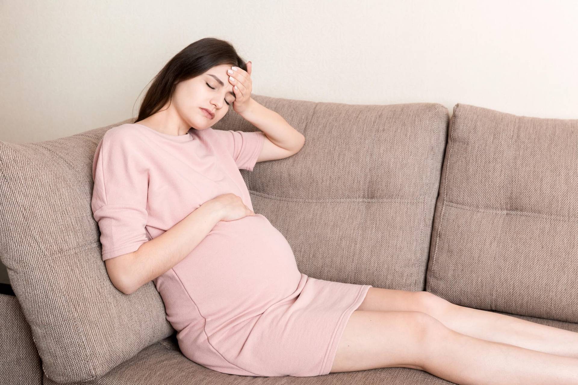 Personne enceinte allongée sur un canapé, une main sur la tempe.