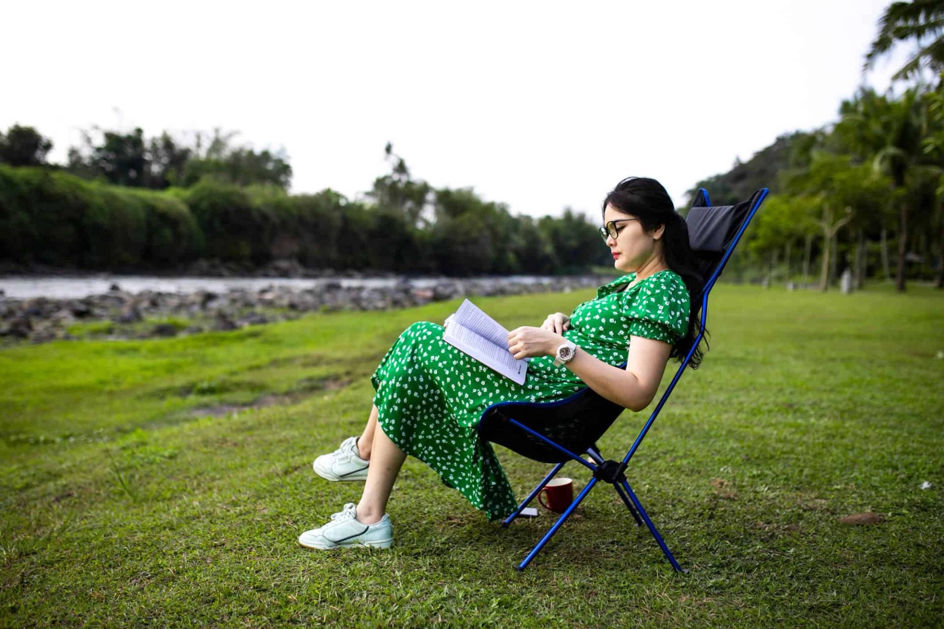 Personne enceinte lisant sur une chaise pliante à l’extérieur.