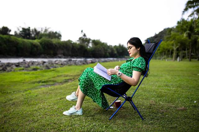 Personne enceinte lisant sur une chaise pliante à l’extérieur.