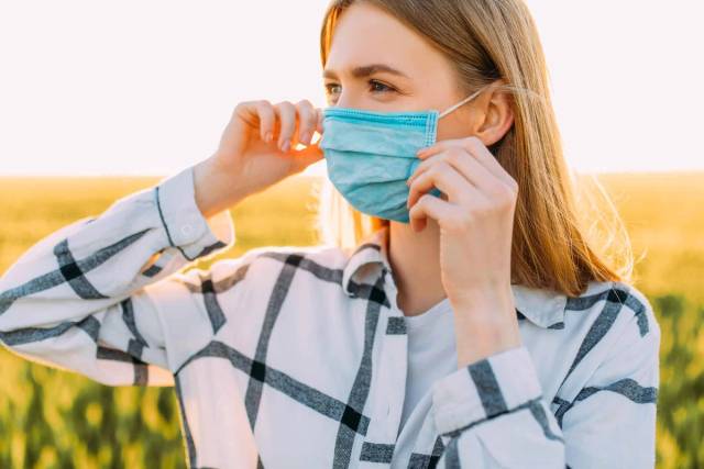 Femme ajustant un masque chirurgical à l’extérieur.