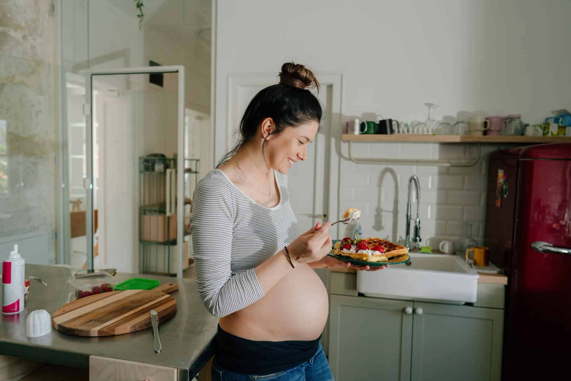 Femme au ventre arrondi devant une salade dans une cuisine.