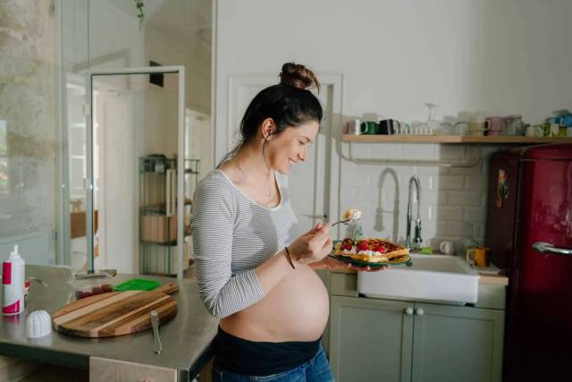 Femme au ventre arrondi devant une salade dans une cuisine.
