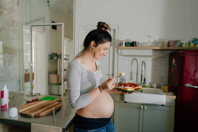 Femme au ventre arrondi devant une salade dans une cuisine.