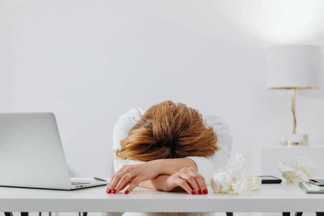 Personne reposant la tête sur ses bras à un bureau avec un ordinateur portable.