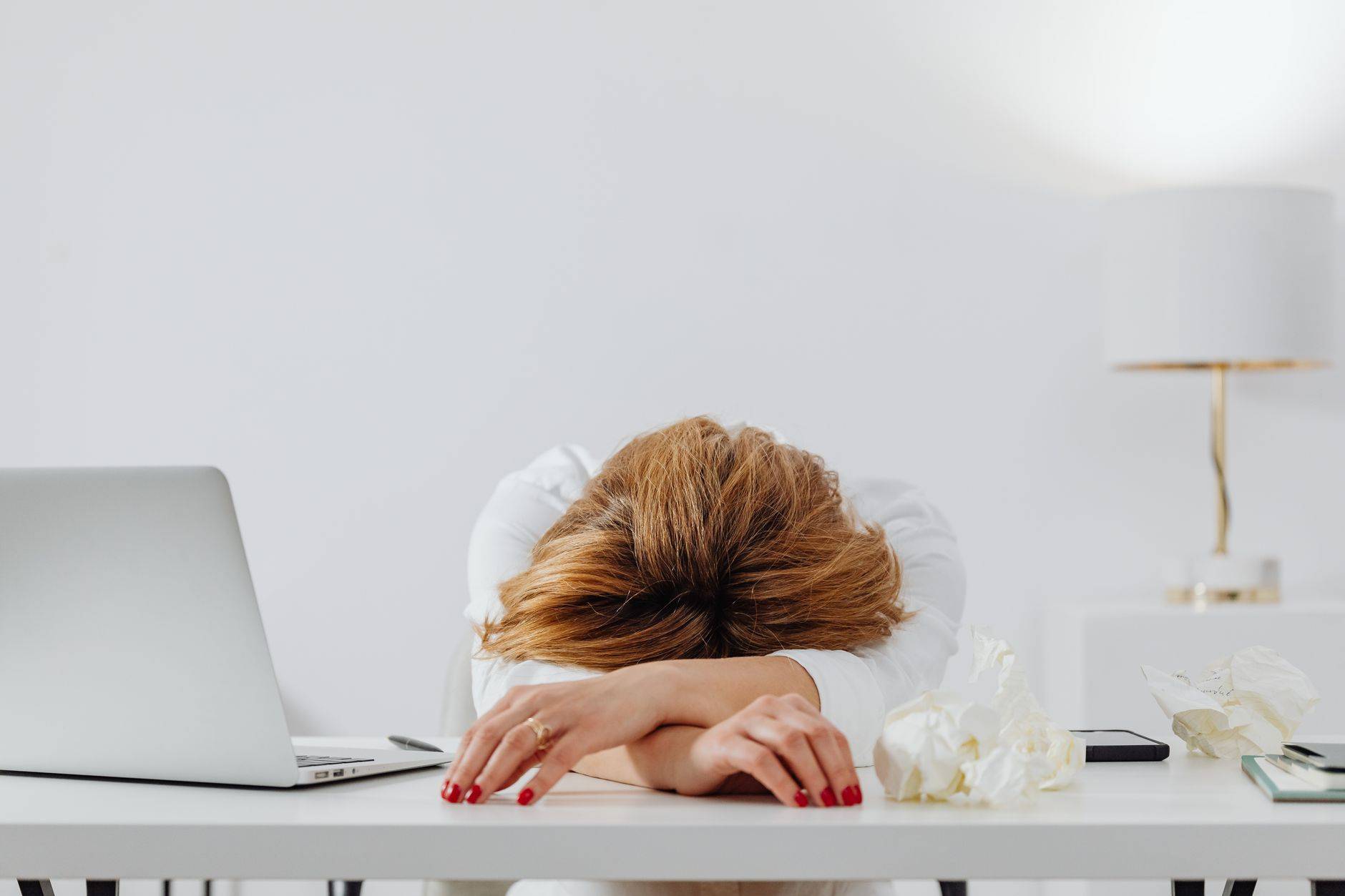 Personne reposant la tête sur ses bras à un bureau avec un ordinateur portable.