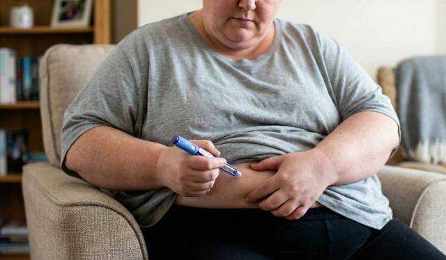 Personne assise utilisant un stylo injectable au niveau du ventre.