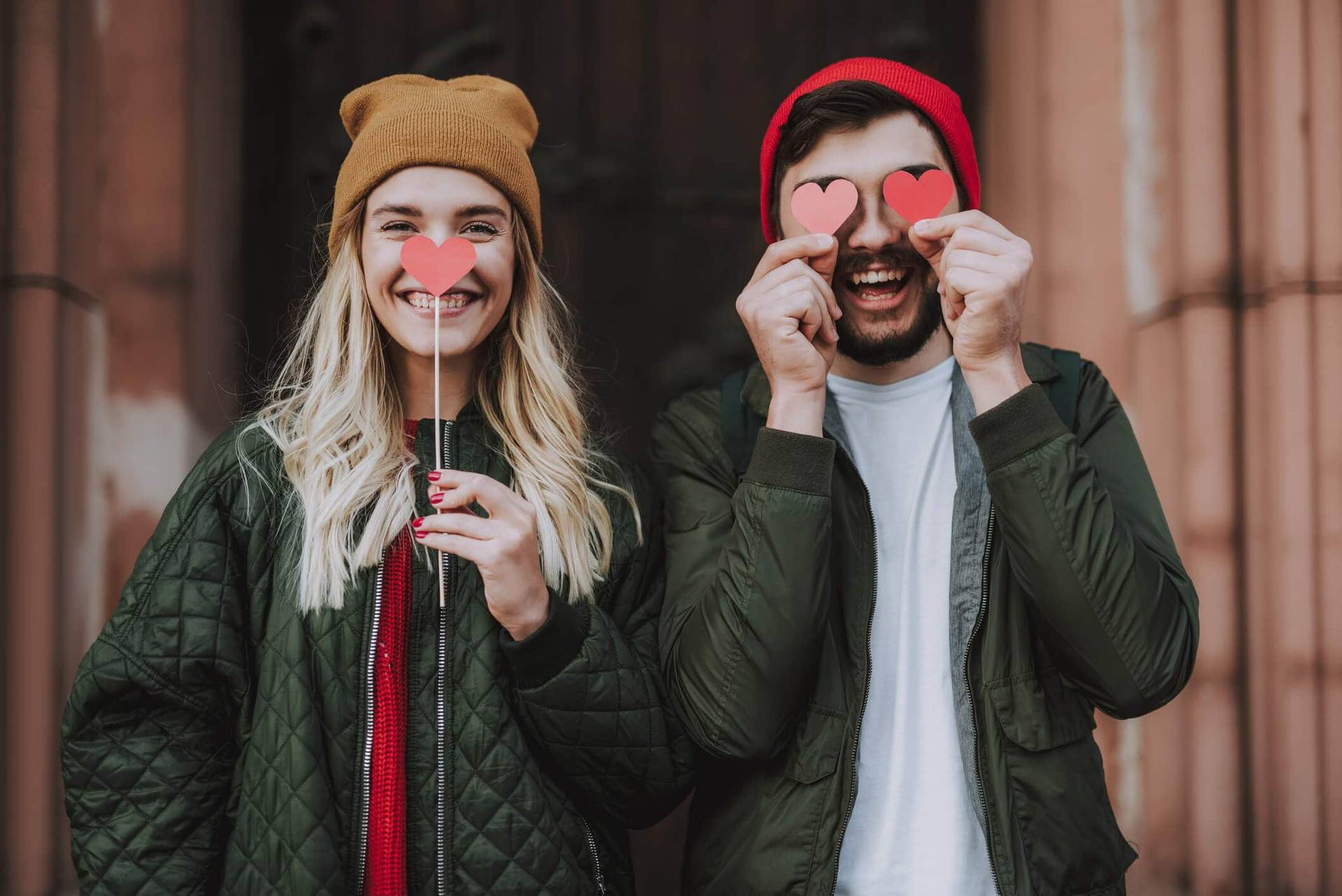 Deux personnes sourianteses tenant de petits cœurs devant leurs visages.