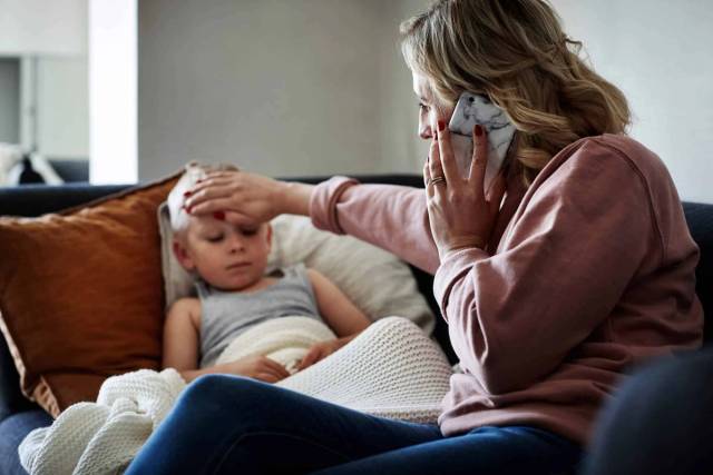 Adulte au téléphone touchant le front d’un enfant allongé.