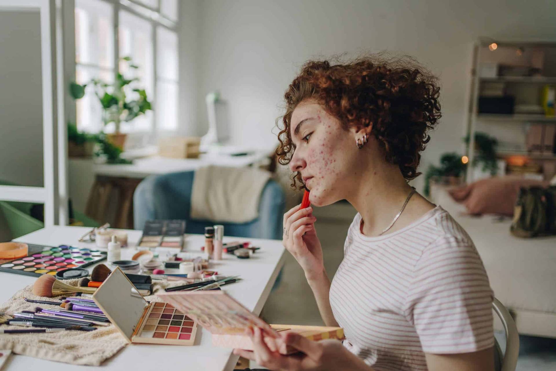 Femme se maquillant devant un miroir posé sur une table.