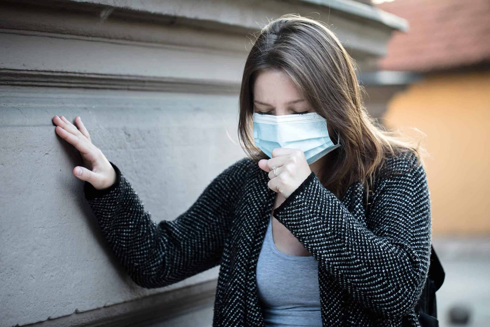 Personne masquée, toussant près d’un mur.