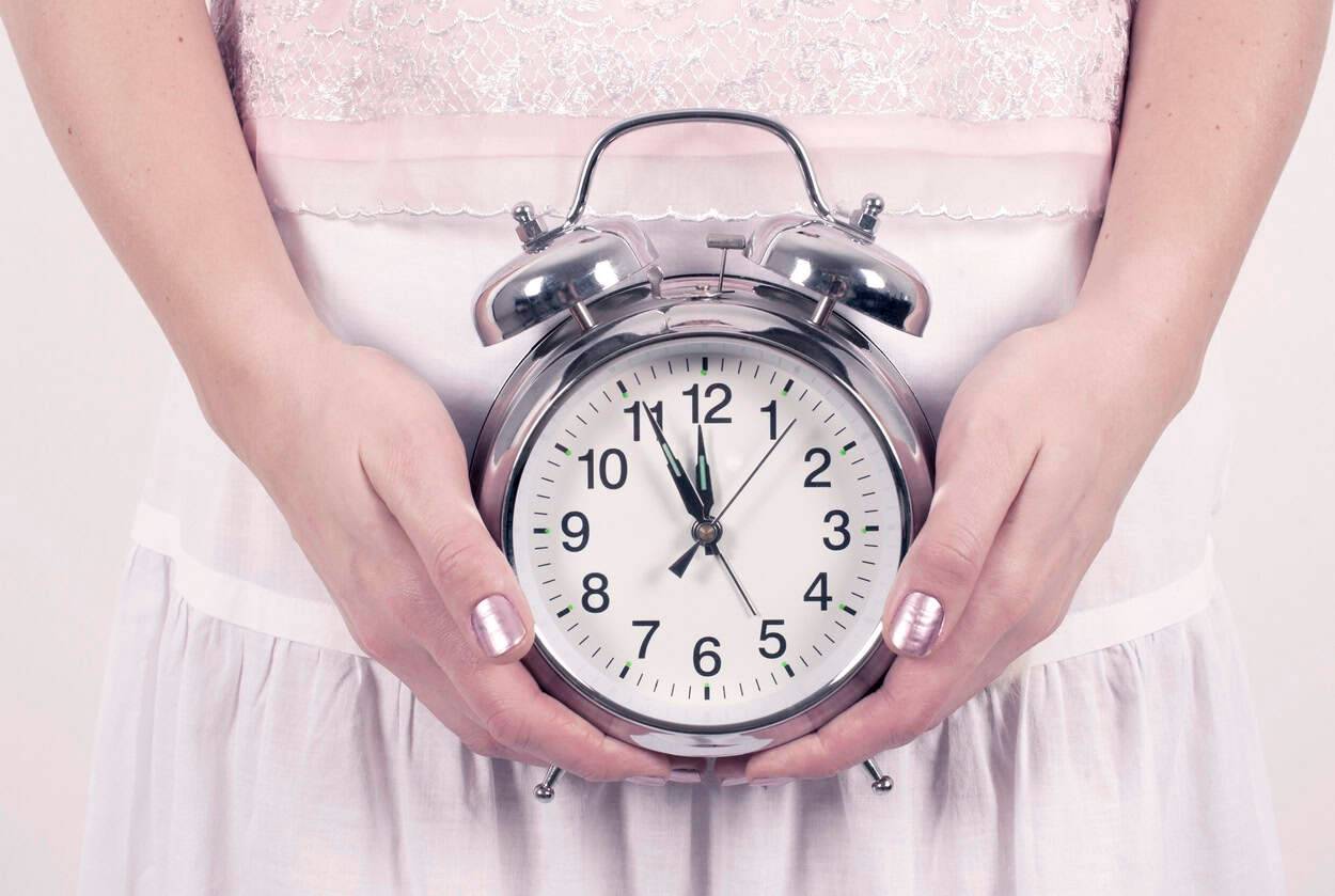 Personne tenant une horloge devant le ventre.