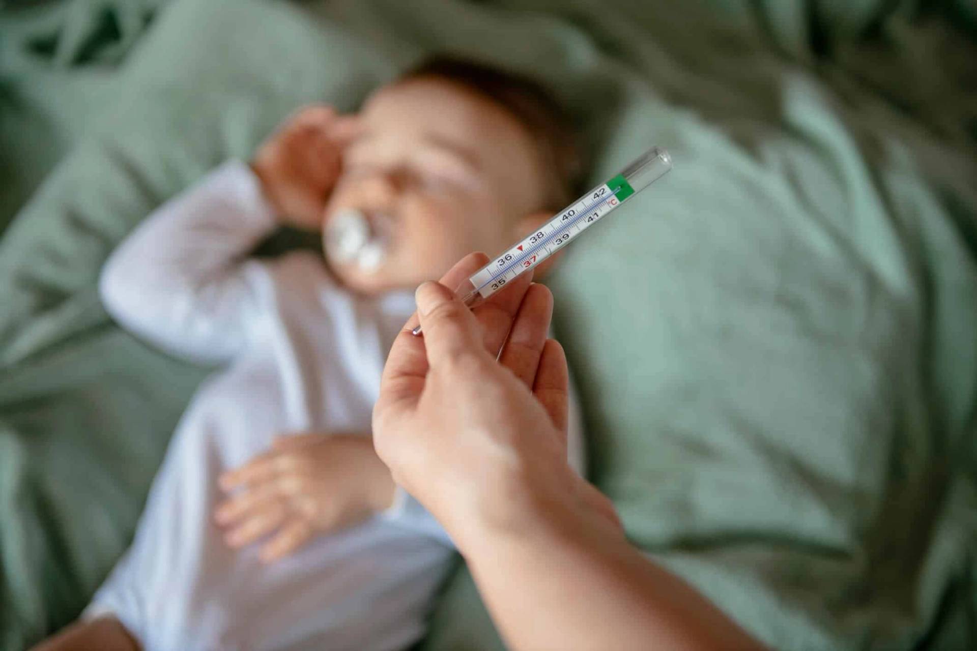 Adulte tenant un thermomètre près d’un enfant couché.
