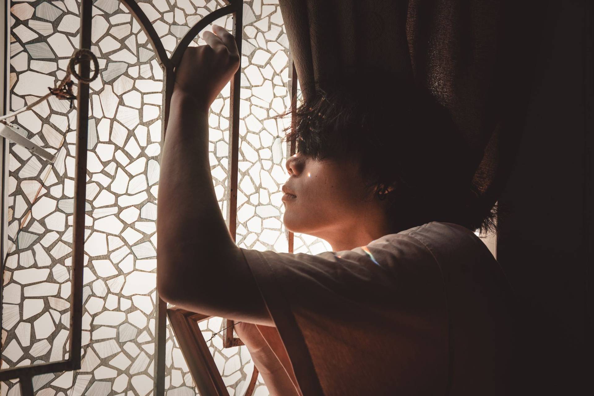 Vue de côté d'un jeune homme posant en réflexion près d'une fenêtre en verre mosaïque avec une lumière douce