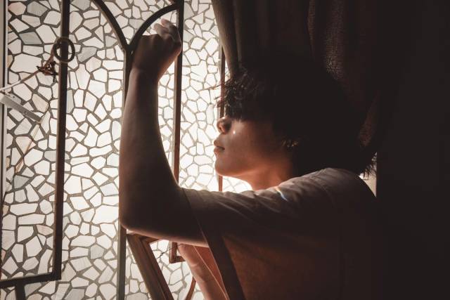 Vue de côté d'un jeune homme posant en réflexion près d'une fenêtre en verre mosaïque avec une lumière douce
