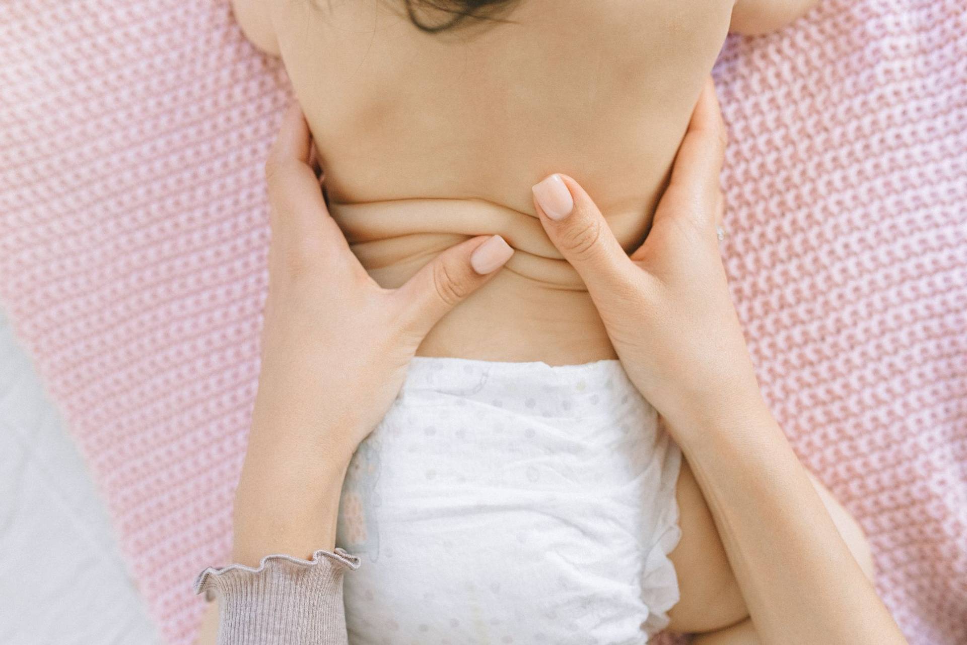 Mains d’un adulte massant doucement le ventre d’un bébé allongé.