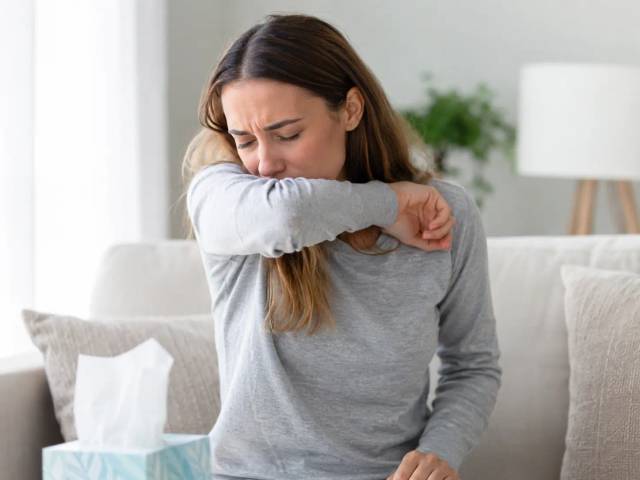 Femme prise d'une quinte de toux allergique, toussant dans le creux de son coude