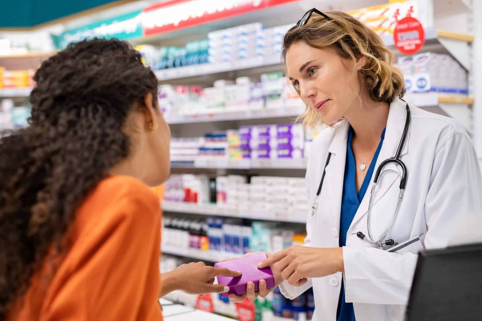 Professionnelle de santé en blouse remettant une boîte à une patiente en pharmacie.