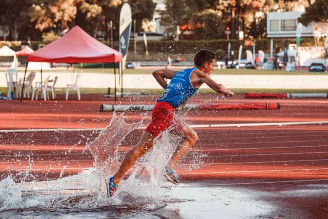 Un athlète masculin courant à travers des éclaboussures d'eau sur la piste lors d'un événement de steeple