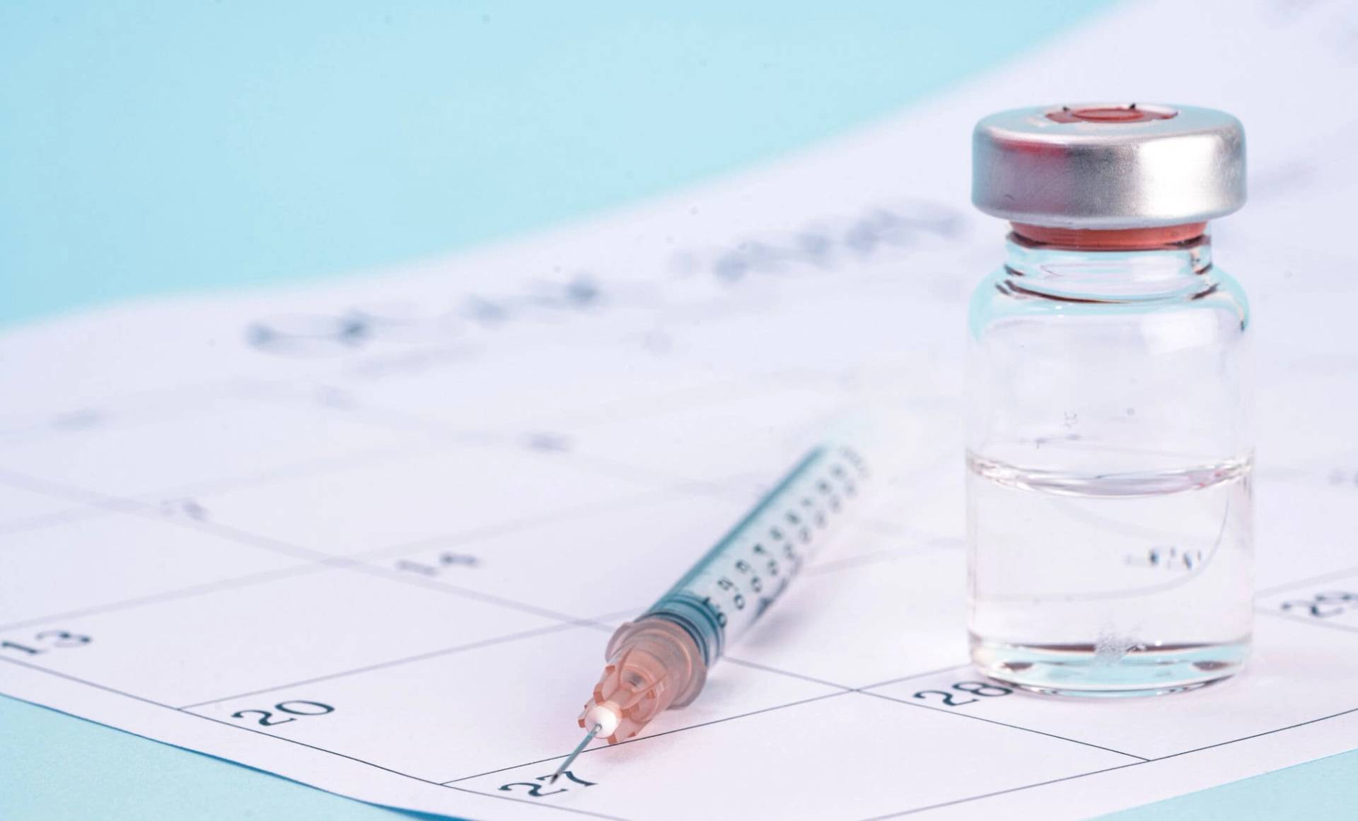 Seringue et flacon de vaccin posés sur un calendrier.