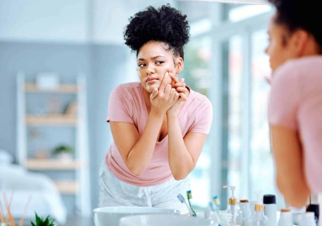 Femme observant son visage dans un miroir.