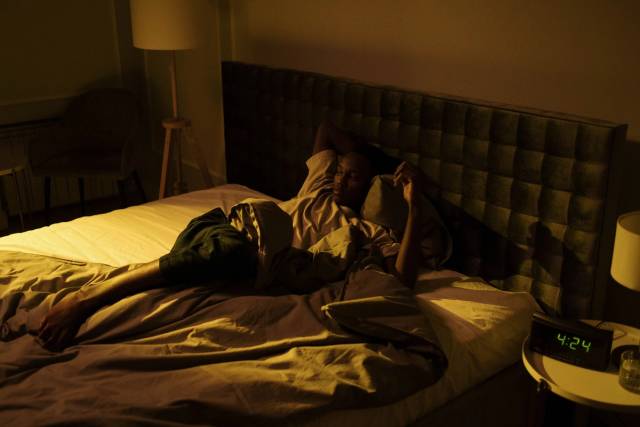 Un homme agité allongé éveillé sur son lit dans une chambre faiblement éclairée la nuit