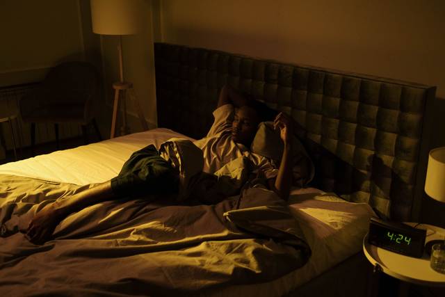 Un homme agité allongé éveillé sur son lit dans une chambre faiblement éclairée la nuit