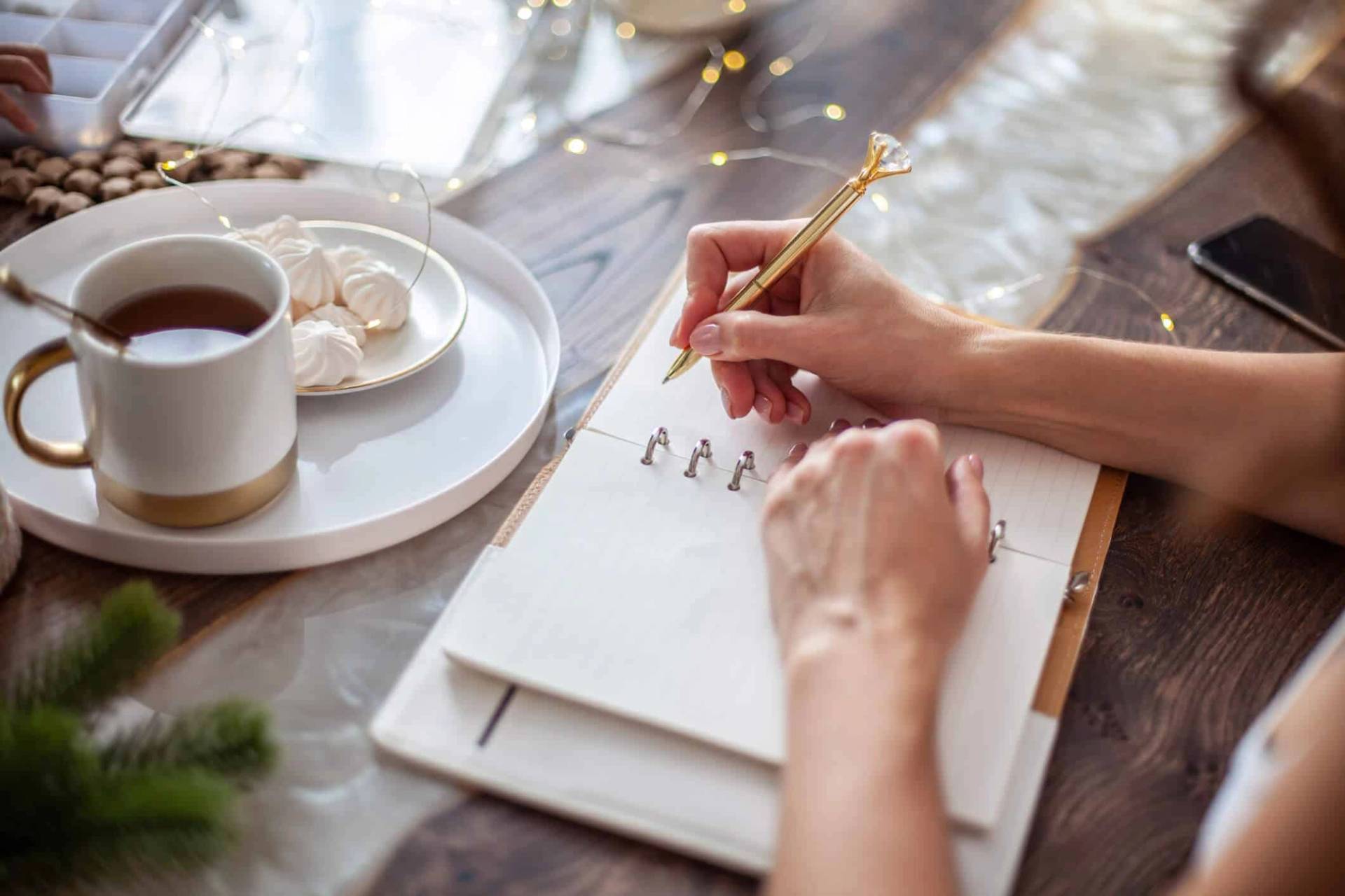 Personne écrivant dans un carnet près d’une tasse de café.