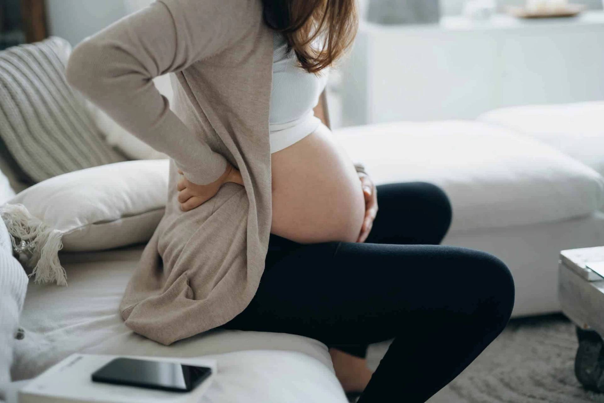Femme enceinte sur un lit, la main dans le dos.