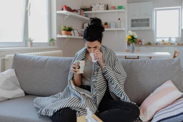 Femme sur un canapé avec couverture, tasse et mouchoir.