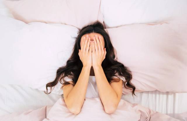 Femme allongée au lit, les mains sur le visage.