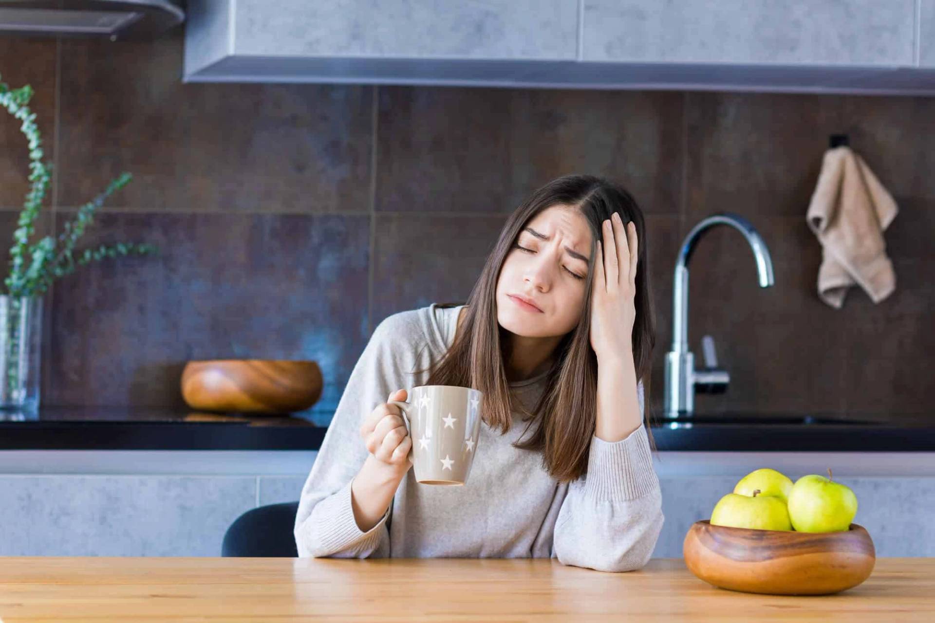 Femme tenant une tasse et posant une main sur sa tête.