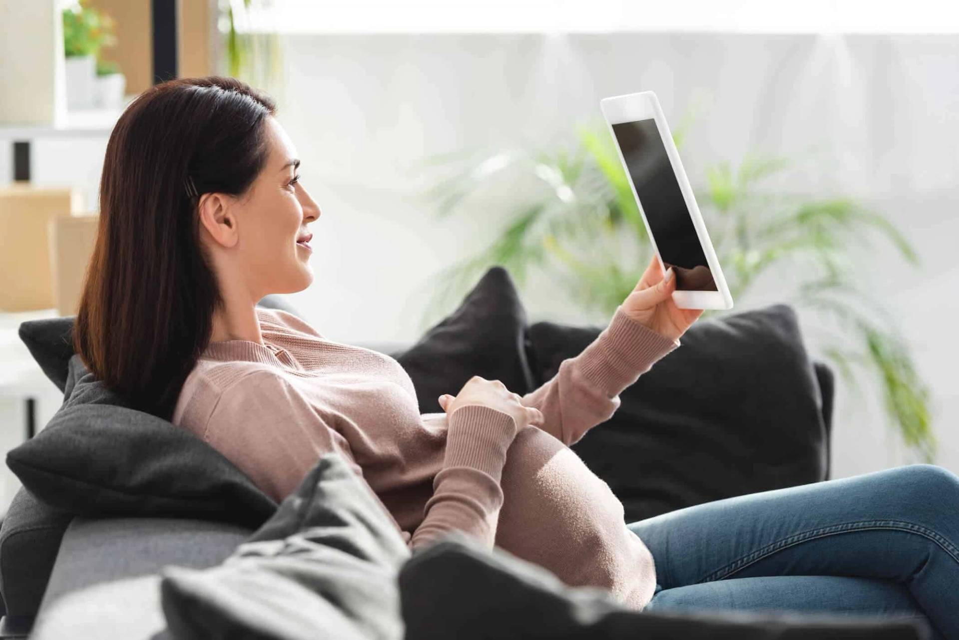 Femme enceinte utilisant une tablette sur un canapé.