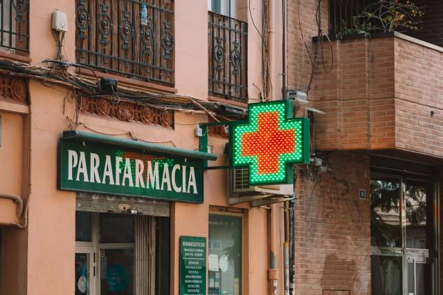 Une vue de rue d'une parapharmacie avec une croix néon lumineuse, présentant l'architecture urbaine des pharmacies