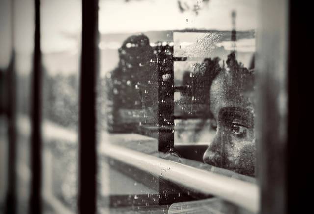 Un enfant, le regard perdu dans ses pensées, regarde à travers une fenêtre ruisselante de pluie
