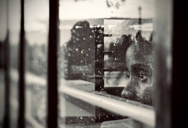 Un enfant, le regard perdu dans ses pensées, regarde à travers une fenêtre ruisselante de pluie
