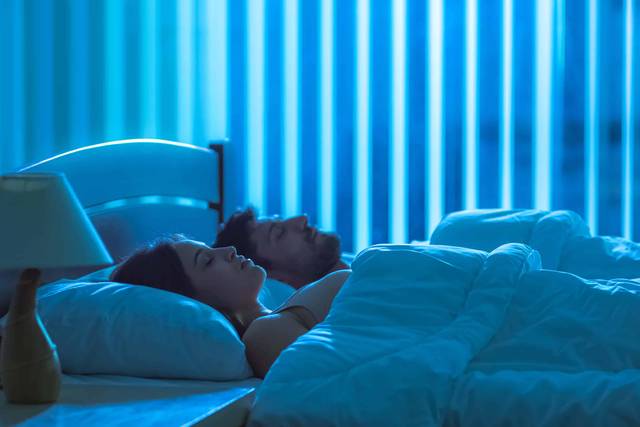 Deux personnes couchées dans une chambre éclairée en bleu.